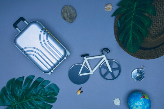 Bicycle travel concept. Suitcase for tourism and recreation with hat and bike on a light background with seashells and compass.