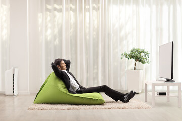 Businessman sitting on a green bean bag chair and watching tv at home