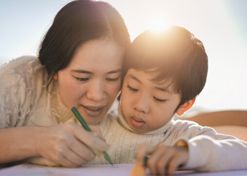 Asian mother doing drawing activities with little son outdoor on patio - Parent and child having fun doing painting activities together