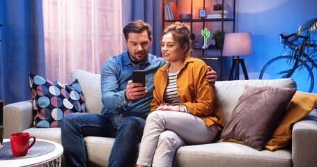 Caucasian young married couple wife and husband resting at home sitting on sofa in modern living...