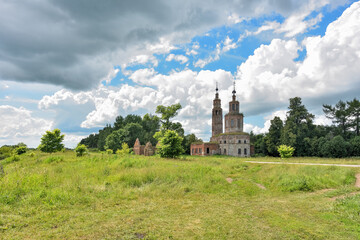 an abandoned dilapidated church, overgrown with grass against the background of the sky, surrounded by greenery
