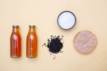 Two bottles of kombucha tea, scoby, brew and bowl of sugar on yellow pastel background. Ingredients for preparing healthy fermented drink. Flatlay mockup