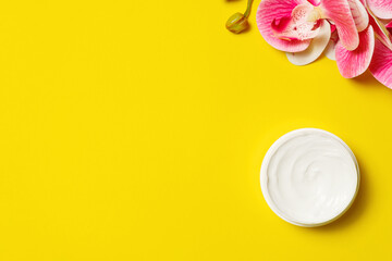 Flat lay of a hand cream and orchid flower on a yellow background. Top view, copy space.