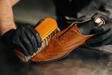 Close-up hands of unrecognizable shoemaker cleaning with brush old light brown leather shoe....