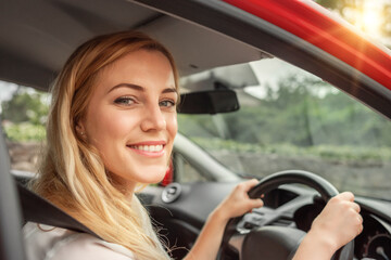Happy beautiful woman is driving a red car.