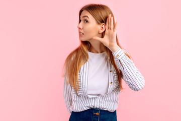 Sly young woman with curiosity listening to gossip or secrets on pink background