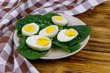 Boiled eggs with fresh spinach leaves and sesame seeds on wooden table