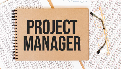 Text PROJECT MANAGER on brown paper notepad on the table with diagram. Business concept