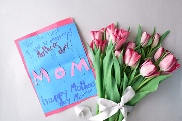 Bouquet of fresh pink tulips and child's handmade Mother's Day card on grey background