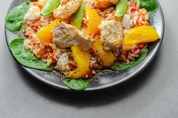Cooked chicken breast pieces with peppers, sugar snap peas, and baby leaf spinach in a spicy sweet and sour sauce with fragrant rice