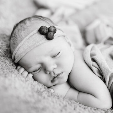 Newborn baby sleeps on blanket. Time to sleep for infant. Tiny baby with beautiful headband lies on the soft violet blanket. Black and white picture