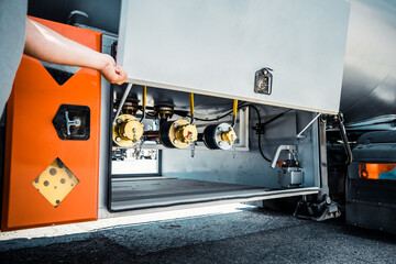 Truck with trailer, tank with flammable liquid, sunny day outside, metallic color container, blue sky with white clouds, gravel