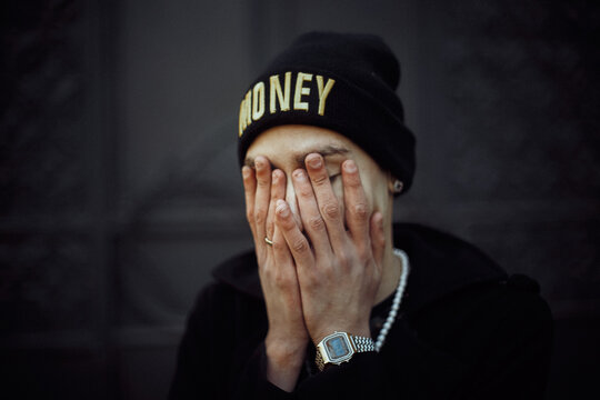 the guy covers his face with his hands in a hat with the inscription money with a Japanese watch in a black hoodie