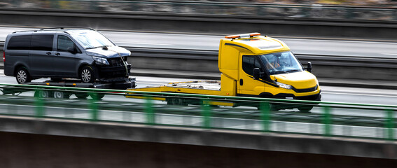 an tow truck with a broken down car speeding on a highway panorama