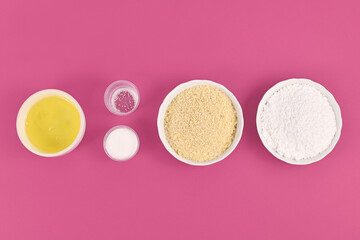 Obraz na płótnie Canvas Bowls with ingredients for making homemade French Macaron sweets showing powdered sugar, ground almonds, egg white, salt and sugar on pink background