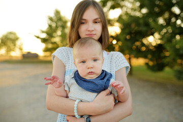 Fototapeta premium Cute big sister admiring her baby brother. Adorable teenage girl holding her new baby boy brother. Kids with large age gap. Big age difference between siblings.