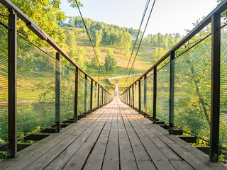 Hanging wooden bridge. Suspension bridge, bridge  against the background of a green meadow and hills.