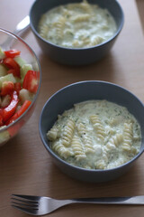 Two bowls of pasta with zucchini sauce and a bowl of cucumber and tomato salad. Selective focus.