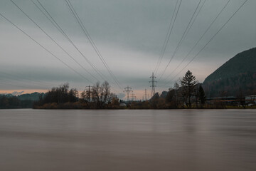 Electricity pillars with wires seen spanning over wild river.