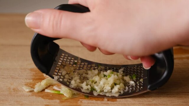 Close Up Shot Of Female Hand Holding The Hand Grater And Crashing The Garlics On The Chopping Board
