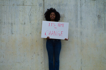 Naklejka na ściany i meble african-american woman with a banner in her hands saying its time to change. In the background grey wall