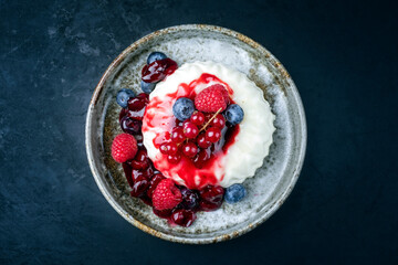 Modern style traditional blancmange almond pudding with wild berry coulis served as top view in a Nordic design plate on black background with copy space
