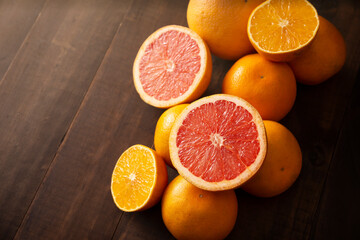 half cut ripe orange and grapefruit and several whole oranges on brown rustic wooden table with...