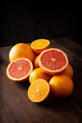 ripe orange and grapefruit slices and several whole oranges on brown rustic wooden table and black background