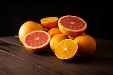 ripe orange and grapefruit slices and several whole oranges on brown rustic wooden table