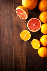 flat lay image of ripe orange and grapefruit slices and several whole oranges on brown rustic wooden table with copy space