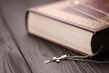 Silver necklace with crucifix cross on christian holy bible book on black wooden table. Asking...