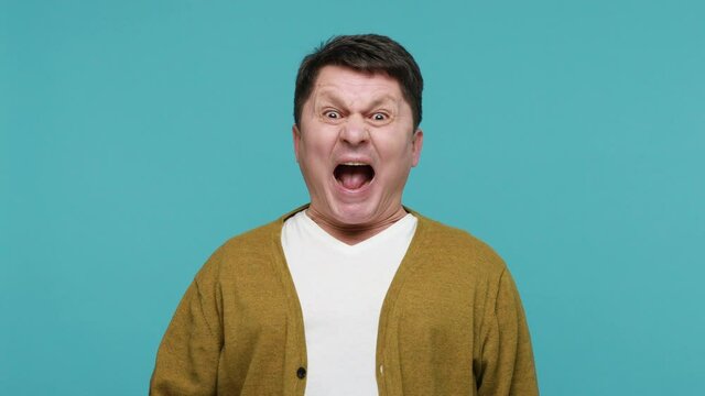 Crazy disobedient middle aged man white t-shirt and cardigan grimacing showing tongue out, fooling faces, bad manners, impoliteness, childish behaviour. Indoor studio shot isolated on blue background