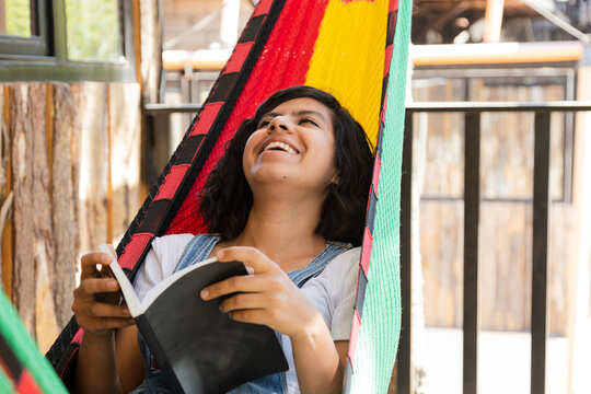 Hispanic young woman laughing in a hammock on the terrace of her house-young woman resting laughing in her country house