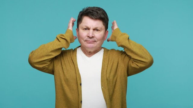 I don't want to hear about this! Nervous annoyed mature man covering ears with hands, rejecting to listen to, avoiding conflict, ignoring problems. Indoor studio shot isolated on blue background