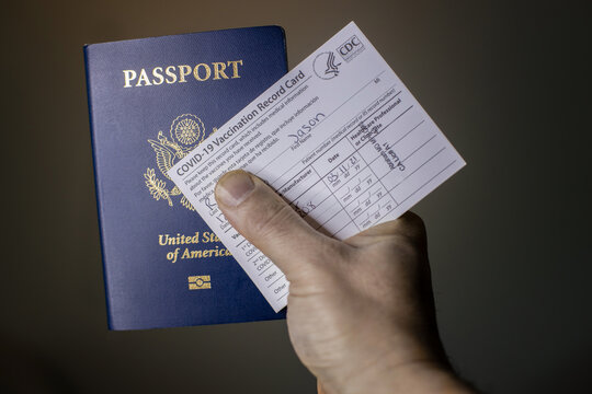 Man's hand holding Passport and Official Covid-19  Vaccination Record Card as a travel pass to travel in the USA or around the World .