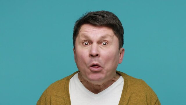 Closeup portrait crazy unhealthy middle aged man crossing eyes and fooling faces showing tongue out, mimicrying and grimacing having fun with silly face. Indoor studio shot isolated on blue background
