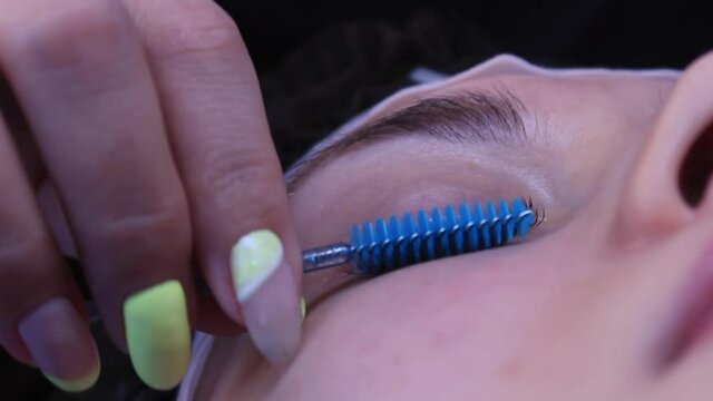 Cosmetologist brushes fake lashes with blue spooly after extentions procedure
