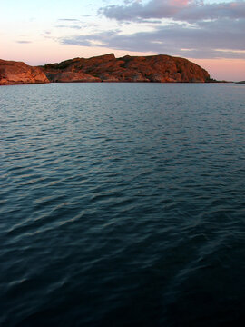 Sunrise in a Norwegian flord, pink and blue sky and sunlit rocks.