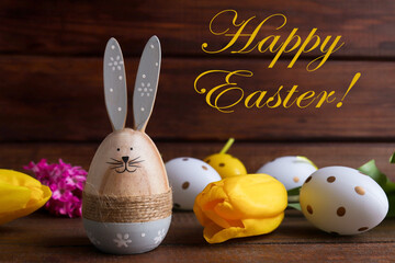 Greeting card. Festive composition with decorative eggs, Easter bunny, tulip flowers and the inscription Happy Easter on a rustic wooden background. Selective focus, close-up