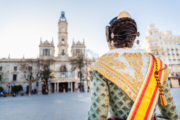 Obraz premium Woman dressed as a Fallera with her back turned, observes the facade of the Valencia City Hall, out of focus in the background.