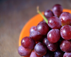 Close view of red grapes on plate on wooden table, close up tight crop perspective.