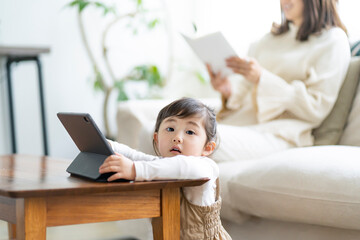タブレットPCを見る日本人の女の子と読書をする母親