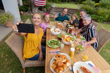 Caucasian woman taking selfie with three generation family having celebration meal in garden