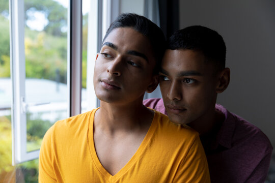 Diverse gay male couple looking through a window and embracing