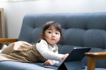 ソファの上でタブレットPCを見る日本人の女の子
