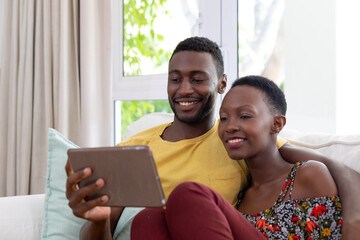 African american couple sitting on sofa using tablet and smiling