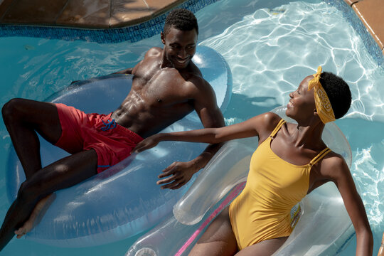 African american couple in swimming pool lying on inflatables and smiling