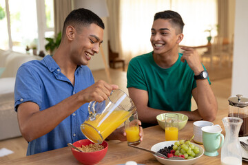 Diverse gay male couple eating breakfast together and talking