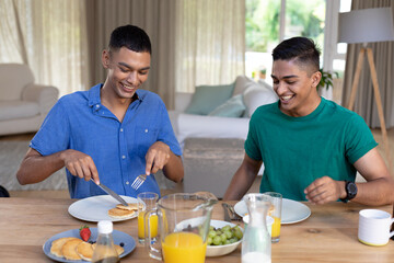 Fototapeta na wymiar Diverse gay male couple eating breakfast together and talking