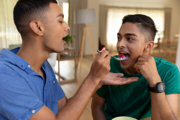 Diverse gay male couple eating breakfast together and talking